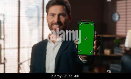 Lächelnder kaukasischer Geschäftsmann mittleren Alters Erwachsener Geschäftsmann Mann männlicher Arbeitgeber Unternehmer im Büro hält Smartphone zeigt Handy grün Stockfoto