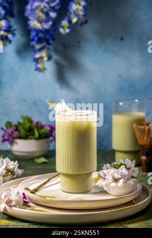 Erfrischendes Matcha Latte Getränk garniert mit zarter weißer Blüte und Minze, serviert in elegantem Glas auf stilvollen Tellern Stockfoto