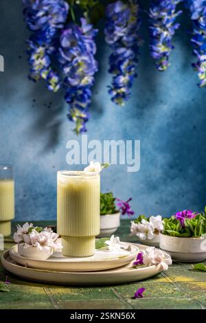 Erfrischender Matcha Latte, garniert mit einer zarten Blume und Minzblatt, serviert auf einem stilvollen Tisch Stockfoto