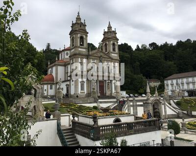 Heiligtum von Bom Jesus do Monte. Barocke Doppeltürme umrahmen eine kunstvoll verzierte Fassade. Treppenaufgang gesäumt von Springbrunnen und Skulpturen zeigen Kreuzstationen. Stockfoto
