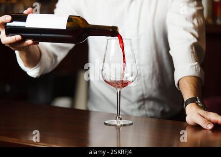 Sommeliermännchen gießt Rotwein in langstielige Weingläser. Stockfoto