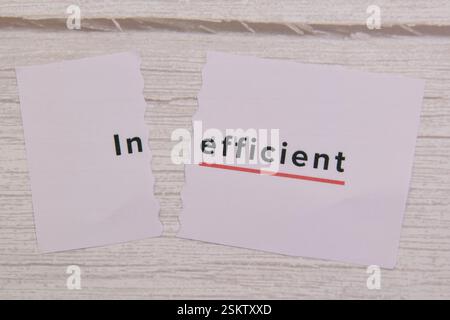 Zerrissene Papierstücke zeigen das Wort ineffizient mit einer roten Unterstreichung auf weißem hölzernem Hintergrund. Stockfoto