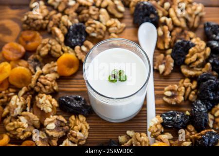 Naturjoghurt mit Nüssen, getrockneten Aprikosen und Pflaumen auf einem Holztisch. Stockfoto