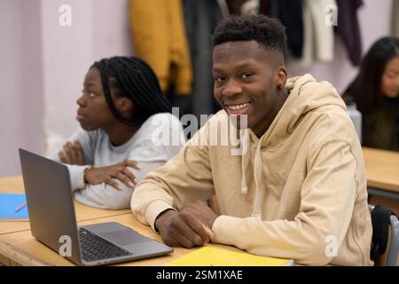 Lächelnder Schüler mit Laptop im Klassenzimmer mit Klassenkameraden, die an der Unterrichtsstunde teilnehmen Stockfoto