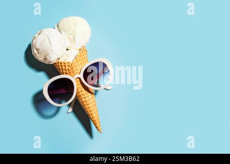 Lustige weiße Eisbecher und Sonnenbrille auf blauem Hintergrund, kreatives Sommerkonzept, Blick von oben, Kopierraum. Trendiger Strand, Entspannung und Sommerurlaub Stockfoto