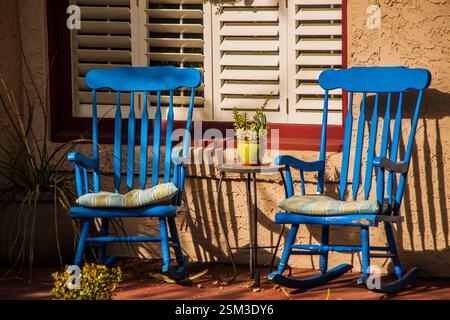 Zwei blaue Schaukelstühle und eine grüne Topfpflanze auf der Veranda einer Residenz. Stockfoto