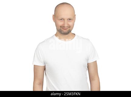 Ein kahlköpfiger Weißer mit kurzem Bart trägt ein weißes T-Shirt und gibt ein dezentes, freundliches Lächeln, während er direkt in die Kamera schaut. Stockfoto