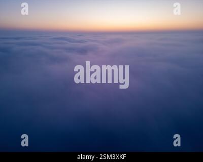Luftaufnahme über Wolken bei Sonnenaufgang, Nebellandschaft in großer Höhe mit rollendem Nebel und goldenem Horizont, atemberaubende Luftaufnahmen im Kino Stockfoto