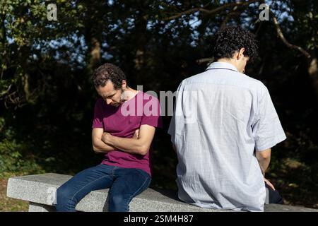 Zwei Männer haben Beziehungsprobleme und fühlen sich wütend und frustriert, während sie auf einer Bank im Park sitzen Stockfoto