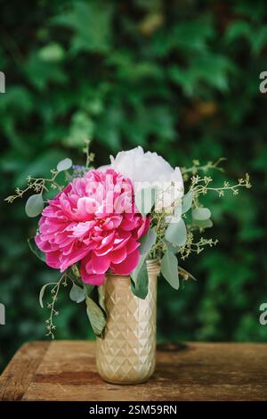 Ein schöner Strauß aus rosa und weißen Pfingstrosen in einer stilvollen Vase verleiht dem Grün einen frischen, lebendigen Touch. Stockfoto