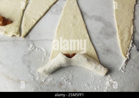 Phasen der Zubereitung eines Croissants. Blätterteig in Rolle wickeln. Stockfoto