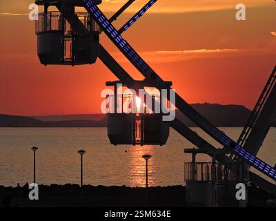 Ein atemberaubender Sonnenuntergang über Prado Beach in Marseille, mit dem Riesenrad, das sich vor dem farbenfrohen Himmel und dem Mittelmeer befindet. Stockfoto
