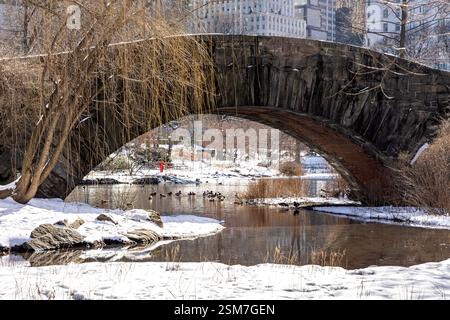 Gapstow Bridge im Central Park mit schneebedecktem Boden und Enten, die einen friedlichen Tag im Teich genießen. Stockfoto
