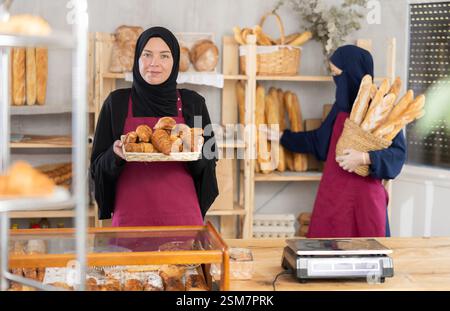 Eine junge muslimische Verkäuferin demonstriert Croissants, während eine andere Frau Baguettes vorrät Stockfoto