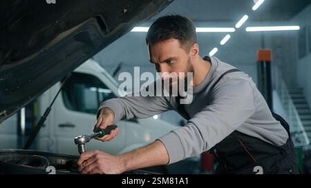 Professioneller Automechaniker Kaukasischer Mann, der in der Fahrzeugwartung arbeitet Motorspezialist, der Motorauto mit einem Schraubenschlüssel fixiert Stockfoto