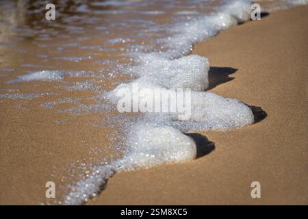 Nahaufnahme von Sea Foam, das sanft über Sandy Beach wäscht Stockfoto