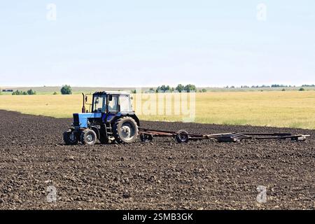 Blauer Radtraktor auf dem Hintergrund von gepflügtem Land, Getreide und Himmel Stockfoto