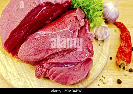 Stücke von Rindfleisch, Knoblauch, Töpfe mit verschiedenen Paprika, getrocknete Chilischote und Dill auf einem Holzbrett Stockfoto