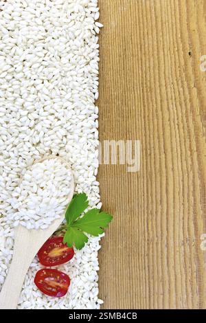 Rahmen aus weißem Reis mit einem Löffel, Tomate und Petersilie auf einem Holzbrett Stockfoto