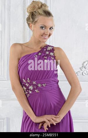 Schöne blonde Frau in lila langem Kleid in weißer Innenausstattung Stockfoto