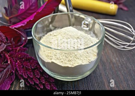Amaranth-Mehl in einem Glasbecher, Mixer, Nudel, Sieb und violette Amaranth-Blüte auf dem Hintergrund von Holzbrettern Stockfoto