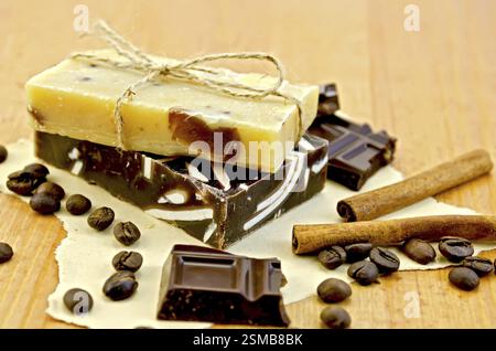 Zwei Takte selbstgemachte Seife, gebunden mit Schnur, Schokolade, Zimt, Kaffee Bohnen auf altem Papier auf dem Hintergrund der Holzbretter Stockfoto