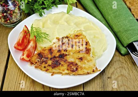 Gebratener Fisch mit Kartoffelpüree, Tomaten auf der Platte, Pfeffer, Petersilie, Serviette auf Holzbrett Stockfoto