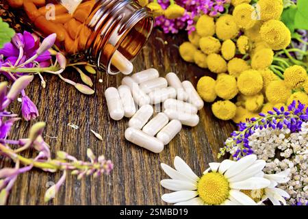 Kapseln in Braun jar öffnen und am Tisch, frische Blumen fireweed, Rainfarn, Kamille, Klee, Schafgarbe, Mädesüß, Minze auf dunklen Holz- Board Stockfoto
