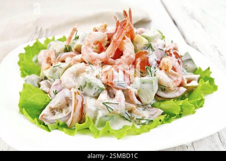Salat mit Garnelen, Avocado, Tomaten und Mayonnaise auf den Salat auf dem Teller, Serviette, Gabel auf Holzbrett Hintergrund Stockfoto