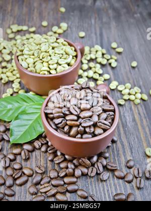 Körner von grünen und schwarzen Kaffee in braun Ton Tassen und auf einem Tisch mit Blättern, die auf dem Hintergrund einer dunklen Holzplatte Stockfoto
