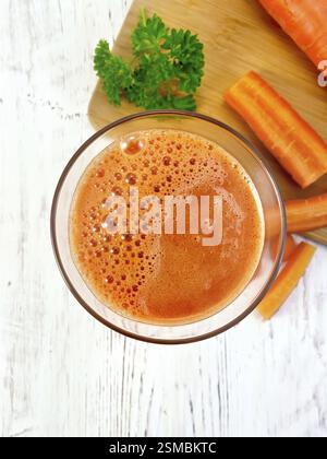 Karottensaft in einem hohen Glas, Gemüse mit Petersilie auf einem Hintergrund aus Holzbrettern oben Stockfoto