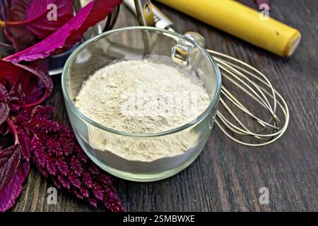 Amaranth Mehl in eine Glasschale mit einem Mixer, ein Nudelholz und Sieb, violette Amaranth Blume auf einem Hintergrund von Holzbrettern Stockfoto