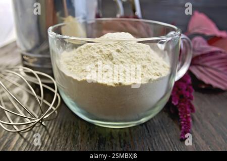 Amaranth Mehl in einem Glasbecher, Mixer und Sieb, lila Amaranth Blüte auf dem Hintergrund von Holzbrettern Stockfoto