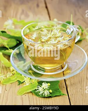 Kräutertee aus Lindenblüten in eine Glasschale, frische Lindenblüten auf einem Holzbrett Stockfoto