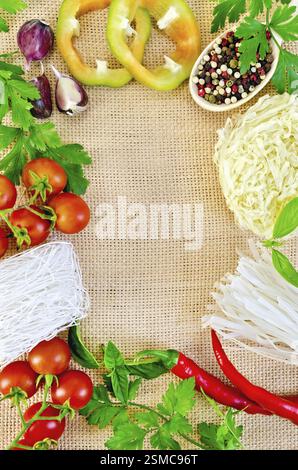 Rahmen aus Reisnudeln, Tomaten, süßen und heißen Paprika, Erbsen verschiedenen Pfeffern in Holzlöffel, Petersilie, Basilikum und Knoblauch auf Absackung Stockfoto