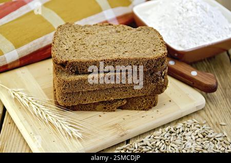 Ein Stapel selbstgemachtes Roggenbrot mit einem Messer und Roggenspikelett auf einem Teller, Serviette, Messer, Mehl und Körner auf einem Holzbrett Stockfoto