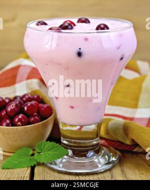 Dicker Joghurt in einem Glasbecher mit Preiselbeeren, Löffel, Serviette, Preiselbeeren in einer Schüssel, Minze auf einem Holzbrett Stockfoto