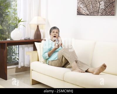 Alte Dame in schockierend Ausdruck hören auf mobile sitzend auf Sofa Herr #702S Stockfoto