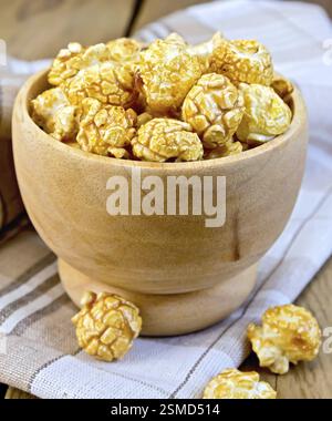 Karamell Popcorn in einer Holzschale auf einer Serviette auf dem Hintergrund von Holzbrettern Stockfoto