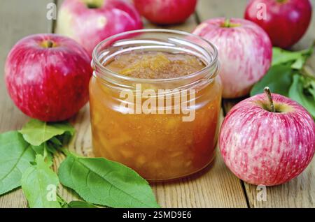Apfel Marmelade in ein Glas, frische rote Äpfel, Zweige mit Blättern auf einem Holzbrett Stockfoto