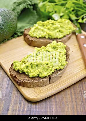 Zwei Scheiben Roggenbrot mit Guakomole, Avocado, Serviette, Petersilie auf dem dunklen Holzbrett Stockfoto