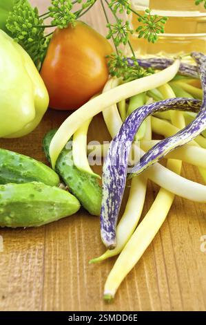 Ein Haufen bunter grüne Bohnen, zwei süße Paprika, drei grüne Gurke, Dill, Regenschirm, eine Flasche Pflanzenöl auf einem Holzbrett Stockfoto