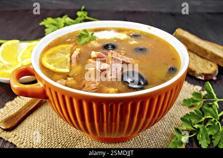 Suppe mit Zitrone saltwort, Fleisch, Gurken, Tomaten Sauce die Oliven in einer Schüssel auf eine Entlassung, Brot und Petersilie auf einem Holzbrett Hintergrund Stockfoto