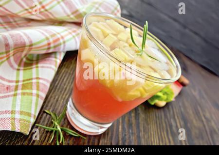 Limonade mit Rhabarber und Rosmarin in einem Glas, Stiele und ein Blatt eines pflanzlichen, kariert Serviette auf einem Holzbrett Hintergrund Stockfoto