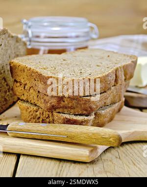 Ein Stapel Scheiben selbstgemachtes Roggenbrot mit einem Messer, Serviette, Brotlaib, ein Glas Honig, Butter auf einem Holzbrett Hintergrund Stockfoto