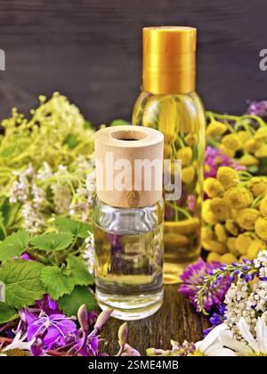 Öl und Lotion Flaschen, fireweed Blumen, Rainfarn, Kamille, Klee, Schafgarbe und Mädesüß, Minze auf einem dunklen Holz- Board Stockfoto
