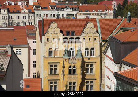 Blick aus der Vogelperspektive auf die Prager Dächer. Rot gekachelte Dächer prägen die Szene mit einigen grünen Akzenten. Ein herausragendes Gebäude mit kunstvoller gelber Fassade und Stockfoto