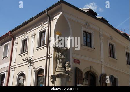 Barocke Skulptur des heiligen Johannes von Nepomuk in einem Eckgebäude. Weißer Halo, raffiniertes Gewand, mit Rosenkranz. Repräsentiert den schutzheiligen der Brücken, Geheimnisse Stockfoto