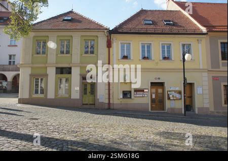 Zwei farbenfrohe Gebäude, eines gelb und eines grün, stehen auf einer kopfsteingepflasterten Straße in der Tschechischen Republik. Das gelbe Gebäude hat mehrere Fenster und einen Stockfoto