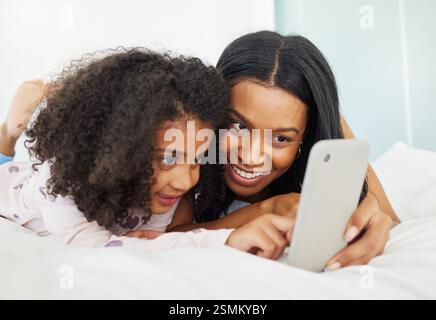 Schlafzimmer, Mutter und Kind mit Smartphone für Video, Streaming-Plattform und Verbindung zu Hause. Haus, Mutter und Mädchen mit Handy zur Bewerbung Stockfoto
